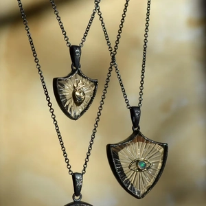 Detail von Schildanhängern mit goldenem Herz und Augenmotiv an schwarzen Ketten