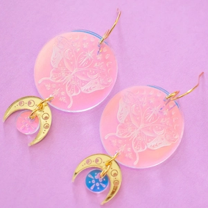 Rosa Schmetterling Acryl-Ohrringe mit goldenen Halbmonden auf lila Hintergrund