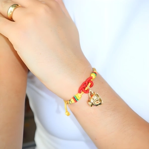 Detail of colorful woven knot bracelet featuring a gold teapot pendant with gemstones