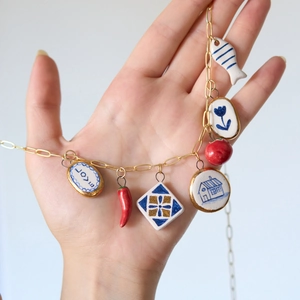 Golden necklace with colorful ceramic charms including fish and tomato in hand