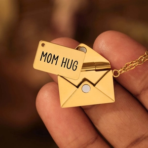 Macro-opname van een gouden envelopketting met gegraveerde MOM HUG tekst aan binnenzijde