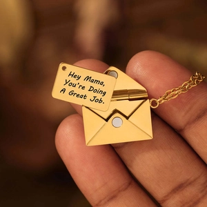 Macro-opname van de gouden envelop ketting met Hey Mama gegraveerde inzetstuk