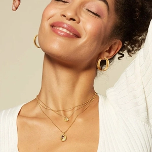 Detail of 18k gold layered necklace with purple stone pendant and textured hoop earrings