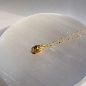 Macro shot of 18k gold stainless steel necklace featuring a green stone in relief pendant
