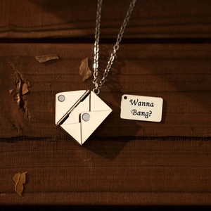 Detailopname van een zilveren envelop hanger ketting met een gegraveerde metalen kaart