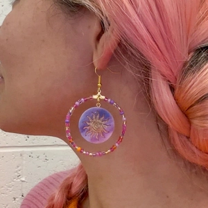 Bohemian beaded hoop earrings with gold sun pendant worn by a model on white background