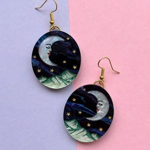 Detail of celestial gold earrings featuring a crescent moon face and blue resin starry sky