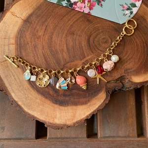 Golden sea theme charm bracelet with pearls, shells and starfish on wood base