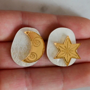 Detail of gold-plated crescent moon and star earrings with white resin and gold glitter