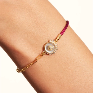 Detalle de pulsera de cadena dorada y cordón rosa con colgante de nácar y piedras de circón
