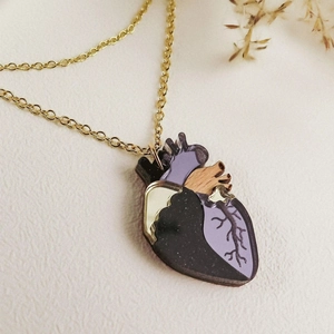 Détail macro du pendentif cœur anatomique violet et noir scintillant sur chaîne dorée