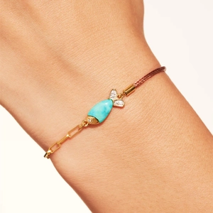 Detalle de una pulsera de pez con incrustaciones de turquesa y cadena de oro en la muñeca