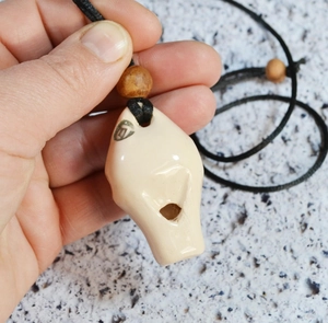 Detail of a creamy white glazed ceramic whistle pendant with wood bead and woven cord