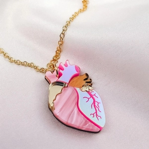 Détail du pendentif cœur coloré avec marbrure rose et chaîne dorée sur satin