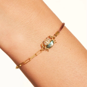 Detalle de una pulsera de cangrejo dorada con incrustaciones de circón y piedra labradorita