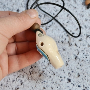 Close-up of handmade ceramic whistle pendant with blue glaze and black woven cord necklace