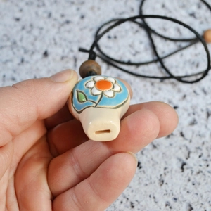 Macro shot of handmade ceramic whistle pendant with blue floral patterns and wooden beads
