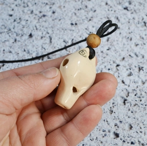 Macro shot of cream ceramic ocarina pendant with green logo and black braided cord