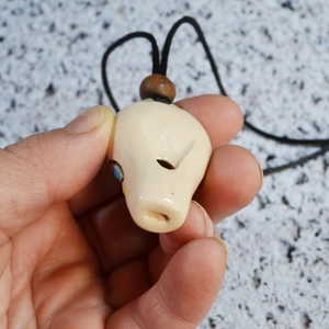 Detail of hand-held bone-like whistle pendant with colorful floral patterns and wooden bead