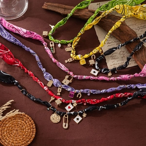 Detail of colorful bohemian silk scarf necklaces with various gold charms on vintage paper