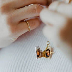 Dettaglio di un medaglione vintage dorato con due foto e un anello sottile in oro e zircone