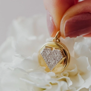 Collana con ciondolo rotondo dorato e cuore in zirconi, tenuta tra le dita