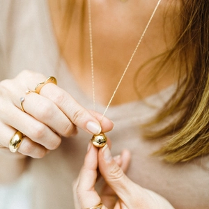 Elegante collana con ciondolo a cuore dorato e anelli d'oro indossati da una modella