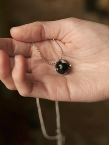 Détail d'une main tenant un collier chaîne argentée avec un pendentif boule noire