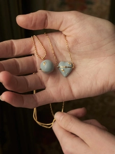 Détail de pendentifs cœur et boule en émail bleu sur chaîne dorée présentés dans la main