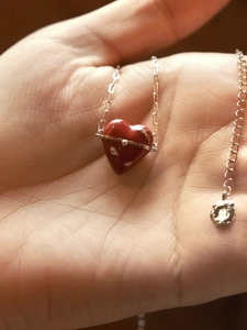 Détail du collier pendentif coeur rouge avec anneau étoilé argenté sur main