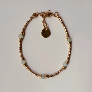 Golden beaded bracelet featuring pale green stone accents and a circular metal charm