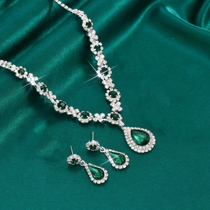 Macro shot of silver jewelry set with pear-shaped emerald gems on dark green silk