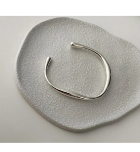 Detailaufnahme des minimalistischen silbernen Armreifens auf weißem Strukturstein