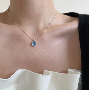 Close-up of elegant oval blue crystal pendant on a silver snake chain worn by a model