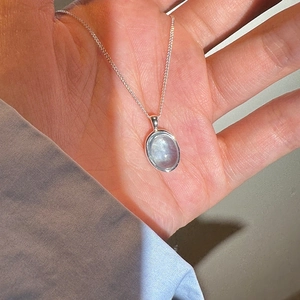Blue oval moonstone pendant necklace with silver chain for women held by hand