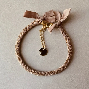 Detail of woven pink satin bracelet featuring gold lobster clasp and adjustable metal chain