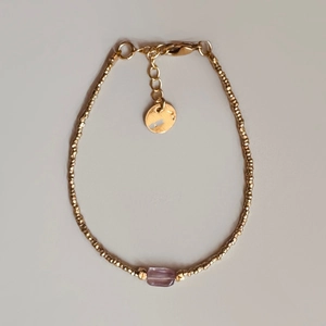 Macro detail of gold beaded bracelet with purple gemstone and lobster clasp closure