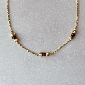 Detailed close-up of bohemian gold chain with reddish-brown garnet beads and metal spacers