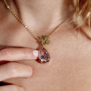 Gold pendant necklace with drop shape dry flower pendant and clover charm on model