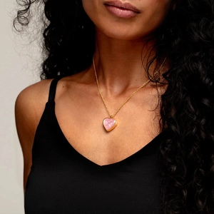 Detalle de collar con colgante de corazón y textura de mármol rosa en una modelo femenina
