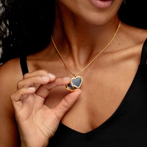 Relicario de corazón en oro de 18k con cadena fina sostenido por la mano