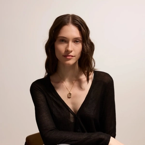 Detalle de un collar dorado minimalista con colgante rectangular en el cuello de una modelo