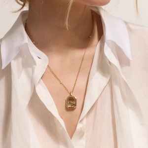 Primer plano de collar de relicario dorado con palmera sobre una camisa blanca