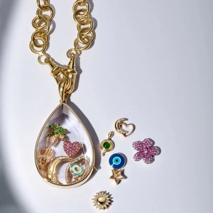 Vista macro della collana con ciondolo a goccia dorata e mini charms in smalto