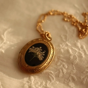 Makroaufnahme eines 14k Gold Medaillons mit echten weißen Trockenblumen und Retro-Ätzung