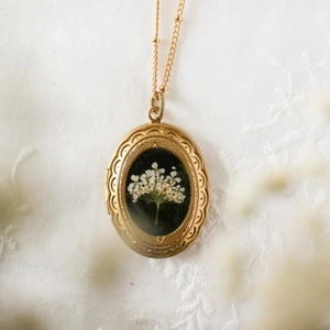 Makro-Detail des goldenen Medaillons mit echten weißen Trockenblumen auf schwarzem Grund