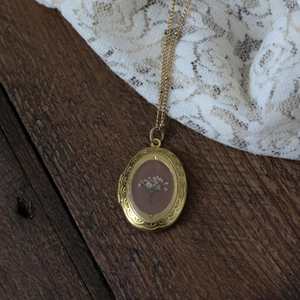 Detailansicht eines ovalen Goldmedaillons mit weißen Trockenblumen und Spitzenstoff