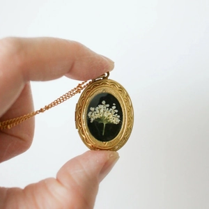Details des goldenen Vintage-Medaillons mit weißen Trockenblumen auf schwarzem Grund