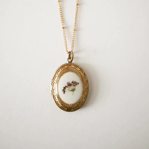 Detailaufnahme eines ovalen 14k Goldmedaillons mit weißen Trockenblumen und Vintage-Stil