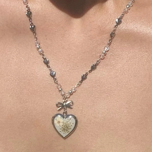 Dettaglio del medaglione a cuore argento con fiori secchi e catena con perline a fiocco